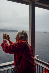 Rear view of woman standing by railing against sea