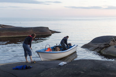 Rear view of woman holding rope while standing on rock formation with man and daughter in motorboat