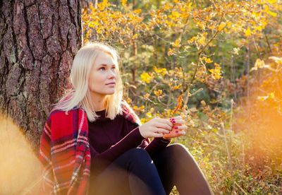 Portrait of young woman sitting in park during autumn