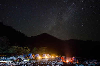 Friends sitting at campfire with tents on field against star field