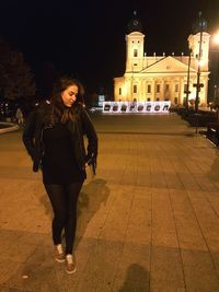 Portrait of smiling young woman standing against illuminated building at night