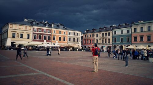 People walking at great market square against cloudy sky during stormy weather