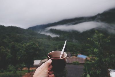 Close-up of hand holding drink against mountain