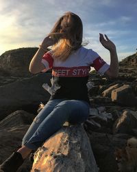 Woman eating food while sitting on rock against sky