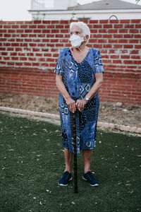 Full length of senior woman holding stick standing against brick wall