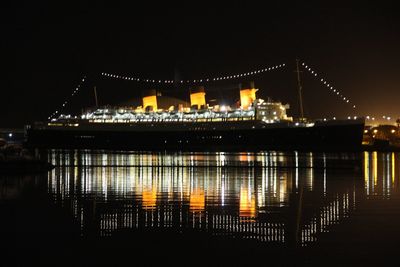 Illuminated buildings by river against sky at night