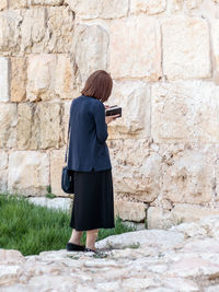 Rear view of woman standing against stone wall