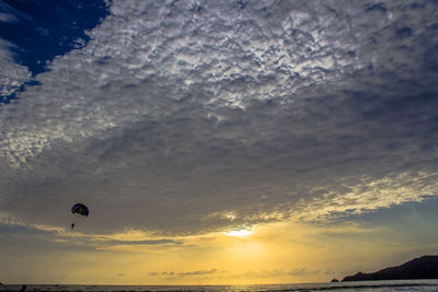 Low angle view of person paragliding against sky during sunset