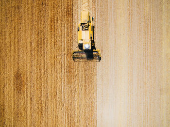 Aerial view of powerful fast yellow vehicle working on field cultivating harvest of wheat
