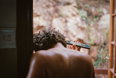 Rear view of shirtless man holding woman at home