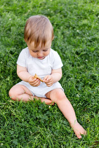 Little baby sits on grass. kid is staring on fallen leaf. outdoor activity on grass lawn.