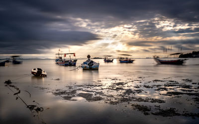 Sailboats moored on sea against sky during sunset