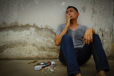 Mature man sitting by narcotics against wall