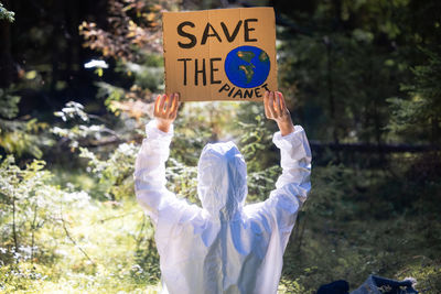 Doctor in a white anti-epidemic suit holding a cardboard banner in hands