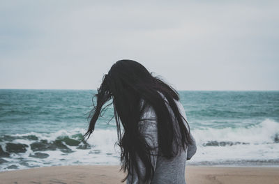 Side view of woman with long hair standing at beach against sky