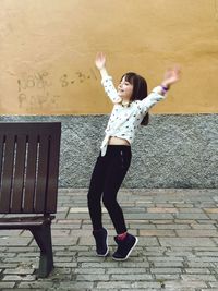 Full length of cheerful girl standing tiptoes against wall