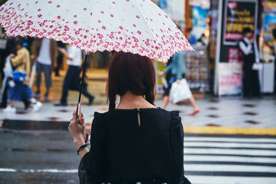 Rear view of woman holding umbrella during rainy season