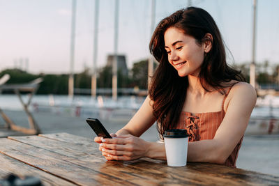 Young woman using mobile phone while sitting on laptop