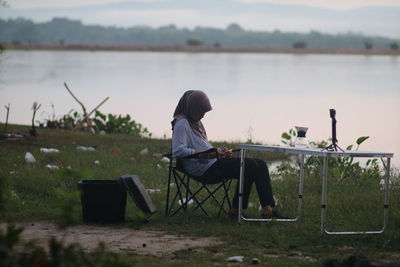 Rear view of man sitting on chair at shore