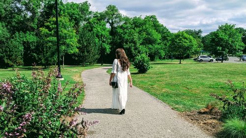 Rear view of woman on field by trees against sky