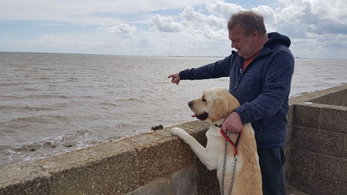 Man with dog pointing at beach against sky