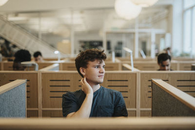 Smiling male student looking away while sitting in library at university