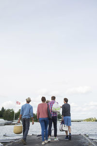 Full length rear view of friends walking on pier against sky