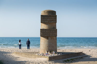 Rear view of people standing on beach against clear sky