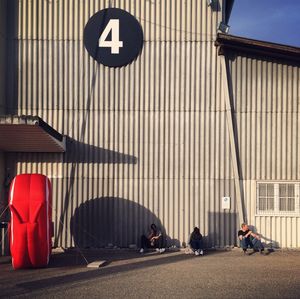 3 people against a wall with number in foreground