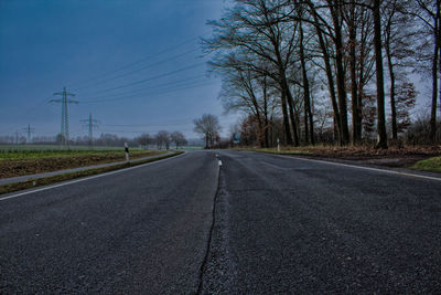 Empty road by trees against sky