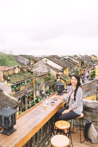 Woman sitting on table by railing against sky