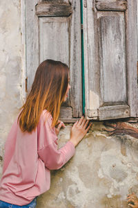 Side view of mid adult woman peeking through wooden window