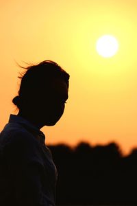 Close-up of young woman against orange sky