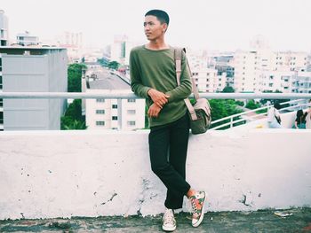 Portrait of young woman standing on retaining wall in city