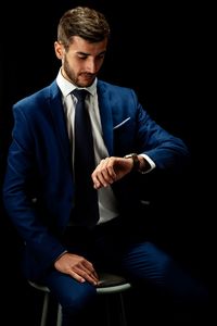 Young businessman in suit sitting against black background