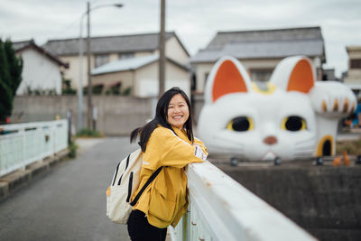 Portrait of smiling woman with backpack standing by railing