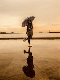 Full length of woman with umbrella standing on beach