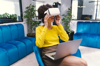 Young businesswoman wearing virtual reality headset while sitting in office lobby