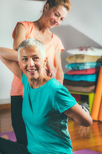 Mid adult daughter assisting mother while practicing yoga at spa