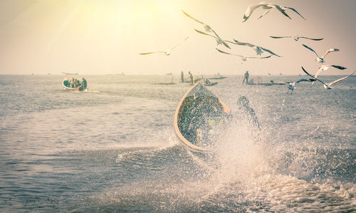 Birds flying over splashing sea against sky