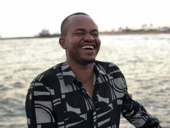 Smiling young man with eyes closed standing against sea during sunset