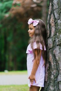 A beautiful girl in a pink dress stands near a tree in the forest and dreams