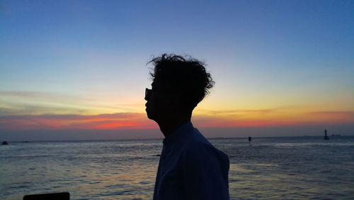 Rear view of silhouette man on sea against sky during sunset