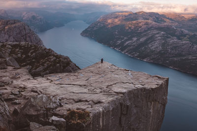 Unrecognizable couple standing at cliff at preikestolen, norway during sunset