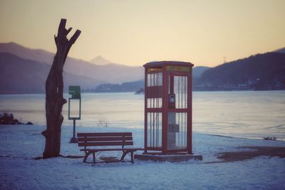 Lifeguard hut on snow covered land against sky during sunset