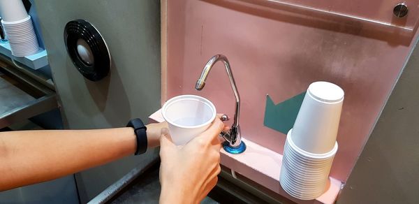 Cropped hands of woman filling water in disposable cup