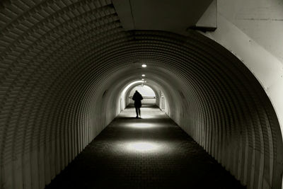 Rear view of man walking in illuminated tunnel