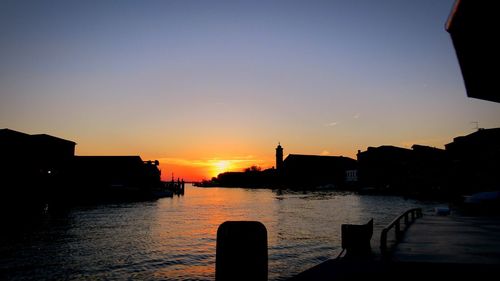 Silhouette buildings against calm sea at sunset