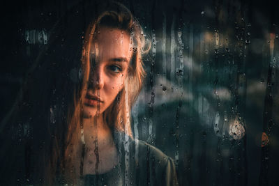 Portrait of woman looking through wet window