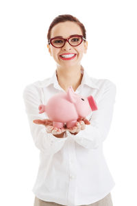 Portrait of smiling young businesswoman holding piggy bank against white background